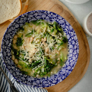 white bean and escarole soup in a bowl with shredded parmesan cheese sprinkled on top