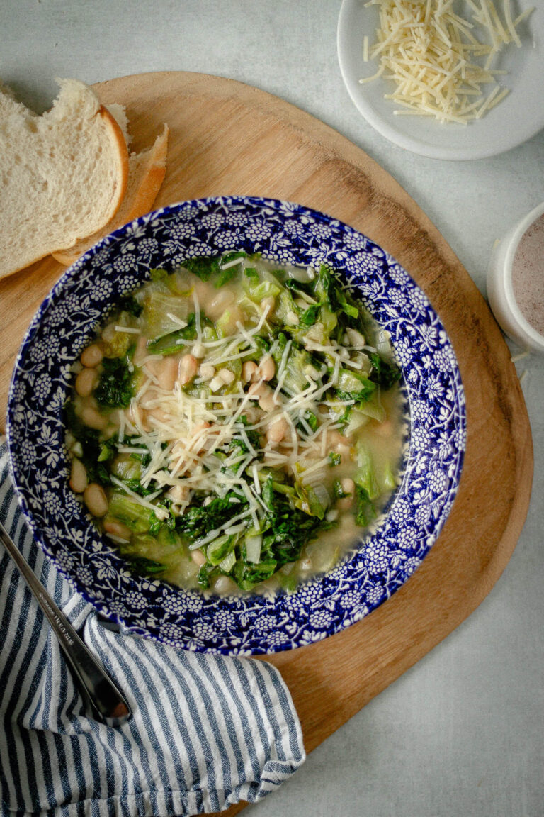 white bean and escarole soup in a bowl with shredded parmesan cheese sprinkled on top