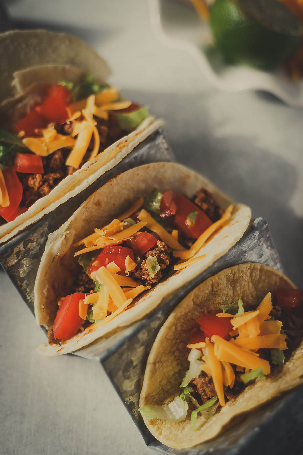 tacos with ground beef, cheese, tomatoes and lettuce wrapped in a corn tortilla
