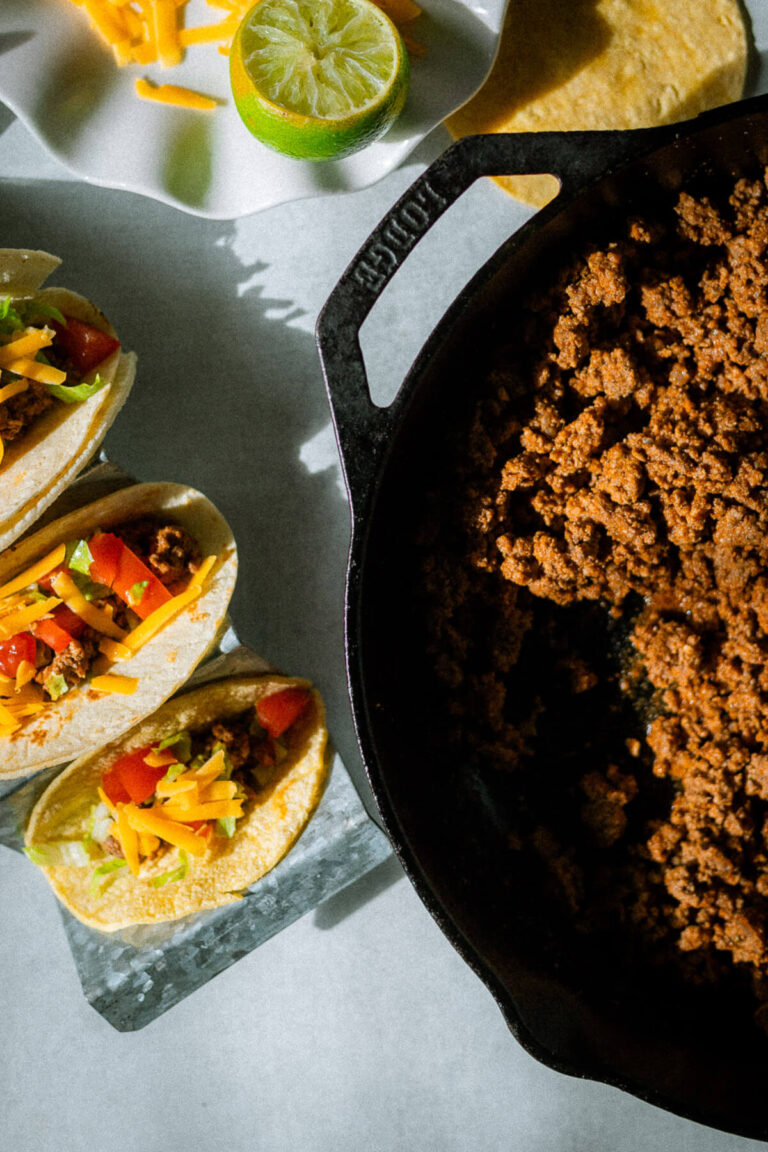ground beef taco meat in a skillet, with tacos with ground beef, cheese, tomatoes and lettuce wrapped in a corn tortilla