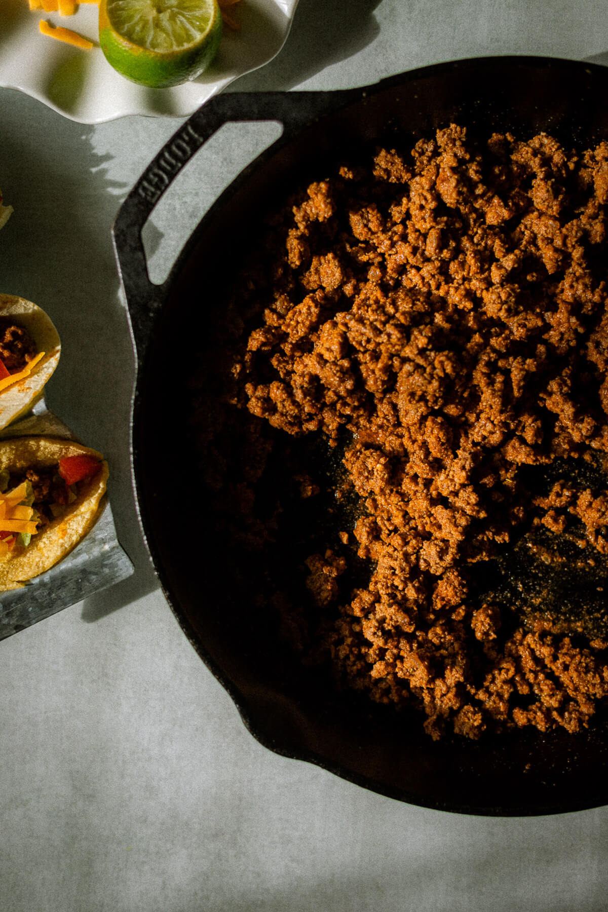 ground beef taco meat in a skillet, with tacos with ground beef, cheese, tomatoes and lettuce wrapped in a corn tortilla